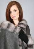 A red haired woman is wearing a medium length grey cape with Indigo Grey fox trim and black leather gloves.