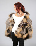 A red haired woman is wearing a medium length taupe cape with Cross Fox trim and dark brown leather gloves. In this photo the cape is worn with one side off the shoulder