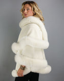 Side view: A blonde woman with green eyes is wearing a medium length off white cape over an ivory turtleneck. In this photo the cape is worn with one side wrapped across the chest and over the opposite shoulder